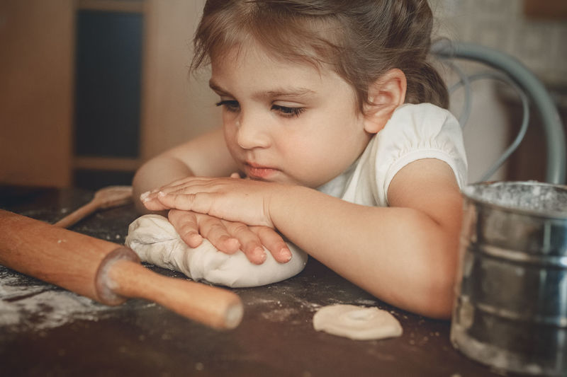 Cute girl sitting at kitchen with dough