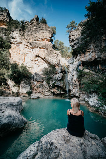 Rear view of woman sitting on rock by rocks