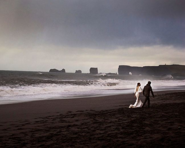 Rear view of bride and bridegroom walking at beach