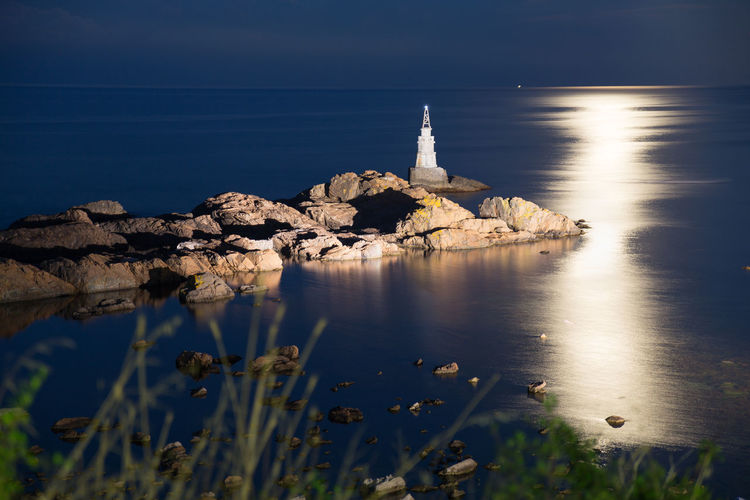 Lighthouse on rock by sea against sky
