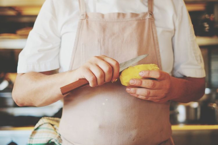 Midsection of chef holding potato and knife in kitchen