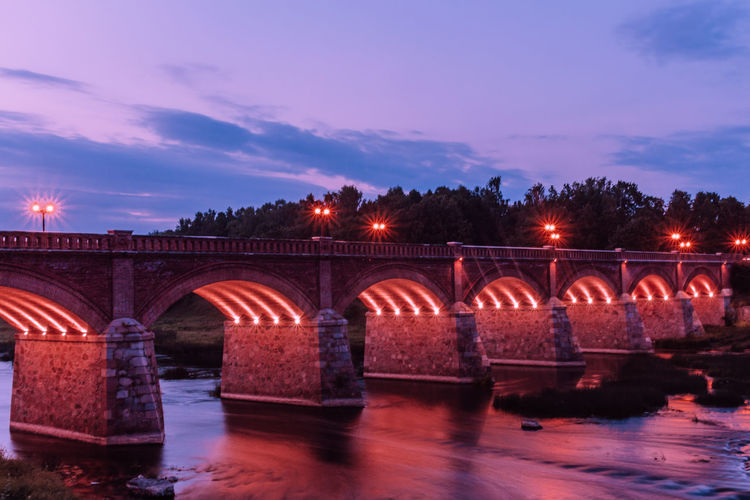 View of illuminated bridge over river against cloudy sky during dusk