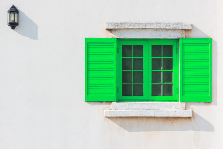 Colorful green window and detail of house exterior on white wall.