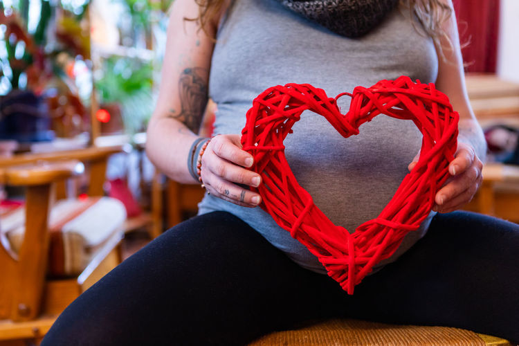 Midsection of woman with heart shape sitting at home