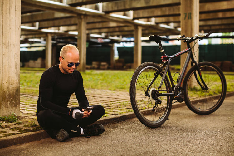 Full length of mid adult man using smart phone while sitting by bicycle