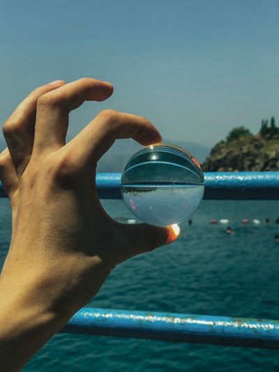 Close-up of hand holding glass against sea