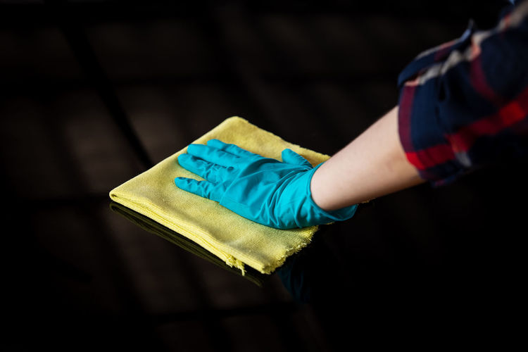 Women worker hand wearing green glove cleaning black car bonnet with yellow microfiber cloth, 