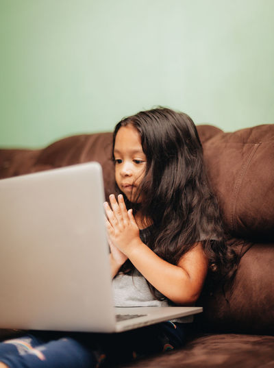 Cute girl using laptop while sitting on sofa at home