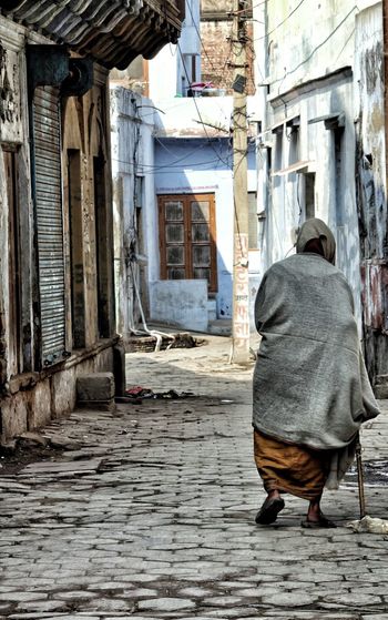 Rear view of poor woman walking in alley