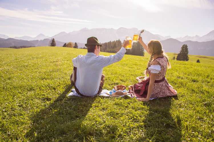 Rear view of couple sitting on field by mountains against sky