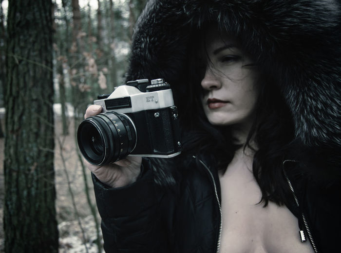 Beautiful fashion model holding camera in forest