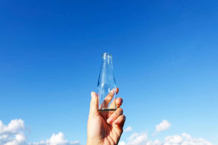 Midsection of person holding bottle against blue sky