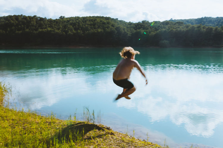 Full length of shirtless boy in lake against sky