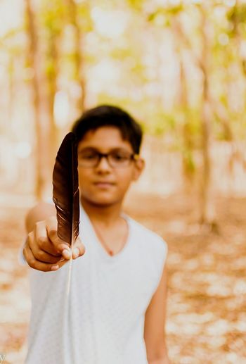 Boy holding feather while standing at forest
