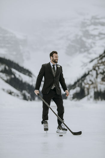 Man in black suit, hockey skates and hockey stick poses on frozen lake