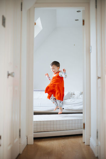 Young boy jumping on the bed in a bright orange dress