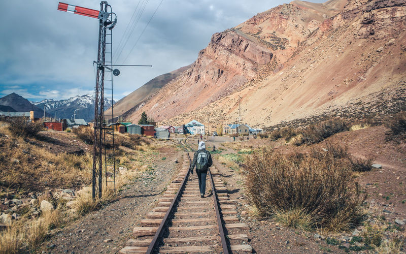 Person walking on railroad track against mountain