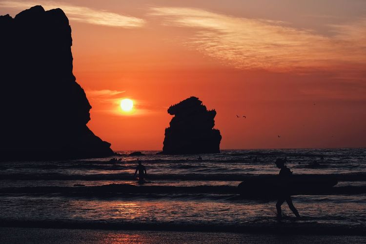 Silhouette rocks on beach against sky during sunset