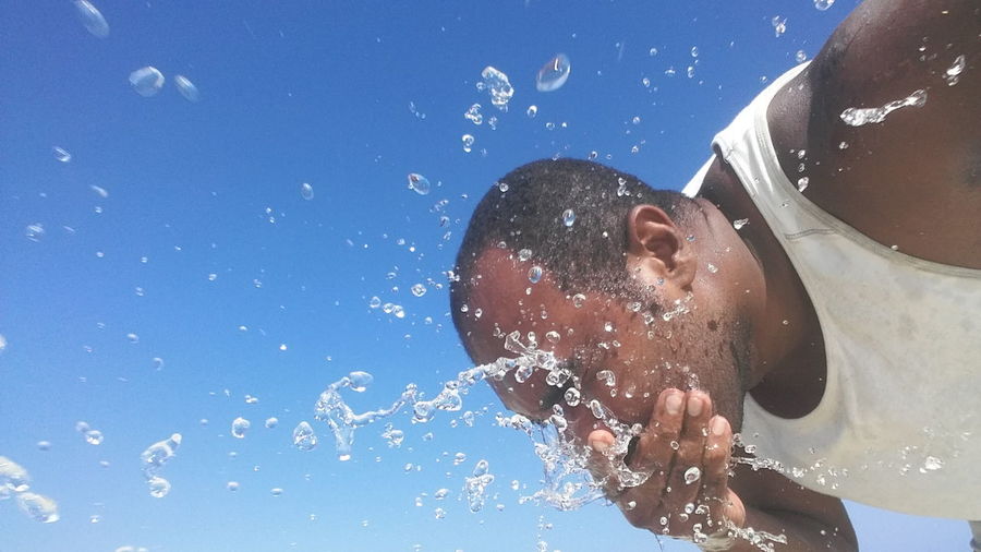 Low angle view of man washing face against sky