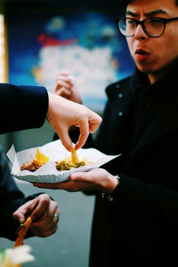 Cropped hand of man having french fries from plate held by friend