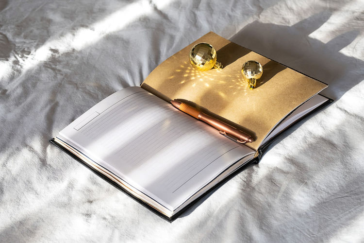 Open notebook, pen and sparkling christmas balls on bed. new year goals. cozy holiday.