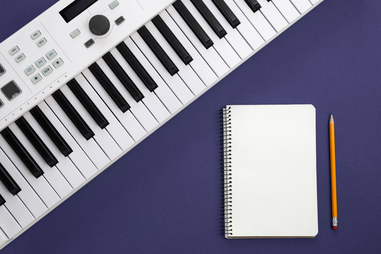Piano keys and blank notepad on purple background, flat lay.