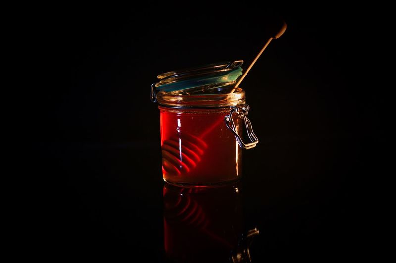 Honey in jar with dipper over black background