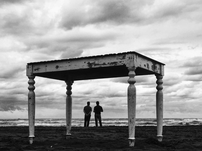 Table against friends standing at beach against cloudy sky