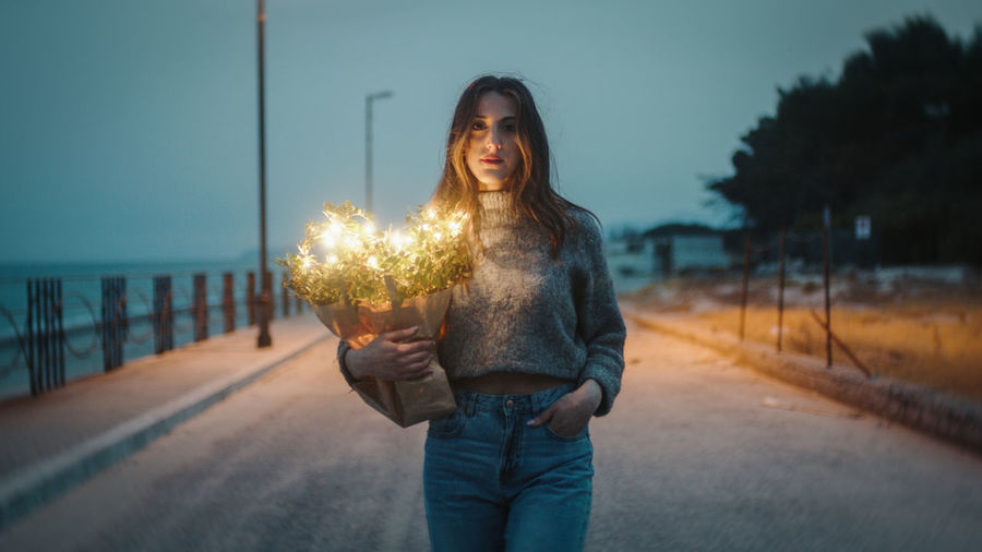 Young girl walks with a bouquet of plants and party lights in her hand