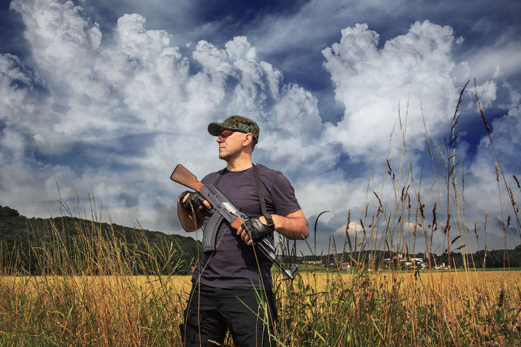 Man holding rifle standing against sky
