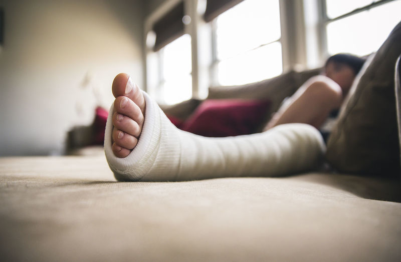 Close-up of boy with fractured leg sitting on sofa at home