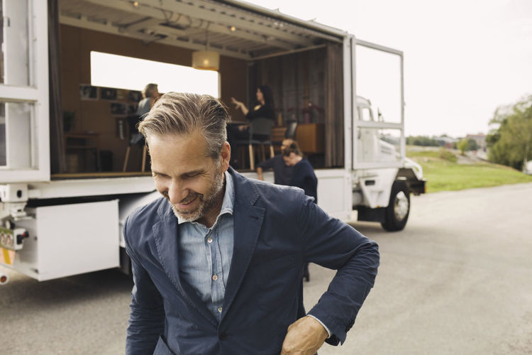 Happy businessman on road with colleagues and portable office truck in background