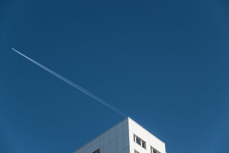 Low angle view of vapor trail over building in clear blue sky