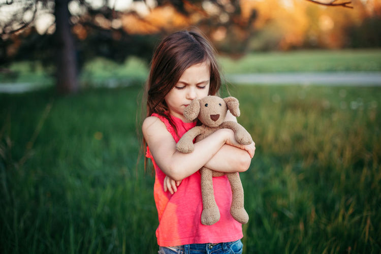 Girl holding stuffed toy and standing on field