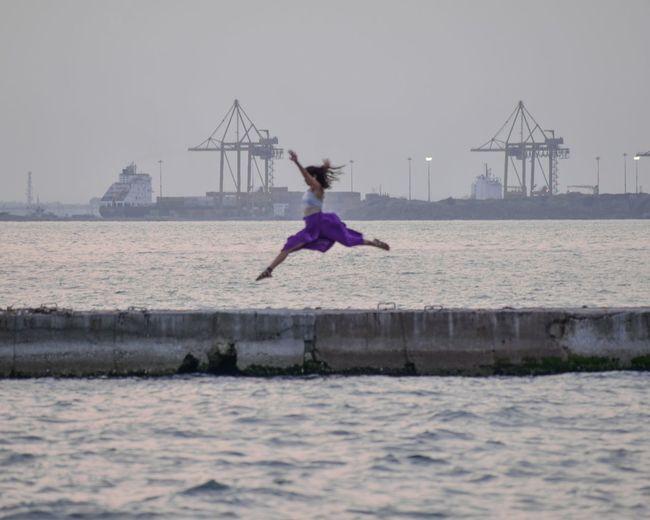 Woman jumping in sea against clear sky