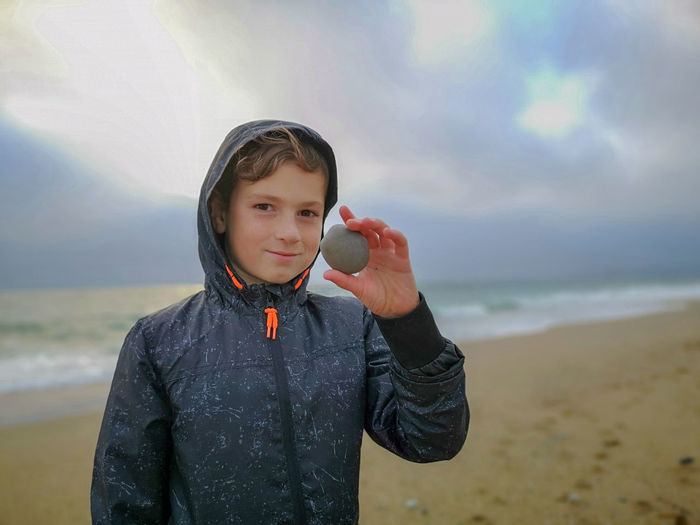 Portrait of smiling boy holding pebble while standing on beach
