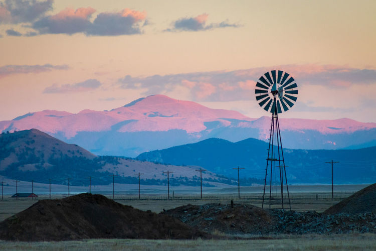 Wind turbines on land against pikes peak and sky during sunset