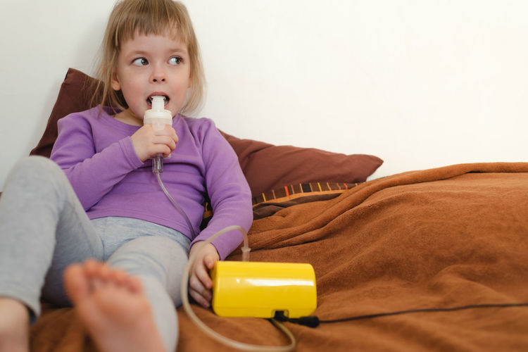 Sick child lies in bed and makes inhalation using a nebulizer.