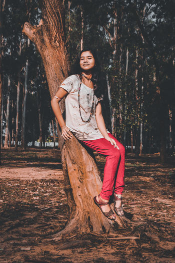 Portrait of smiling young woman on tree trunk
