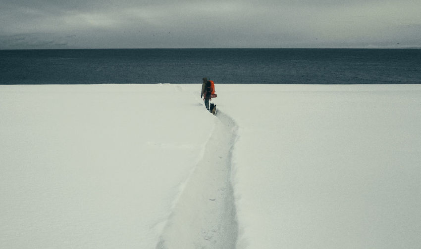 Person on snow covered land by sea against sky