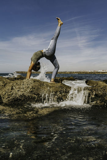 A young women yoga on rock by sea against sky