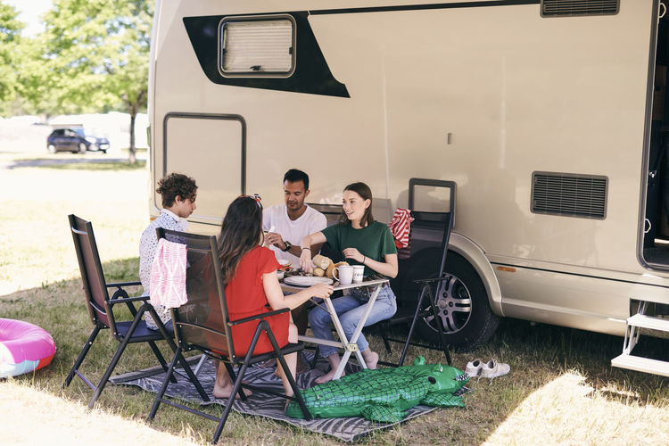 Full length of family having food against van while camping at trailer park