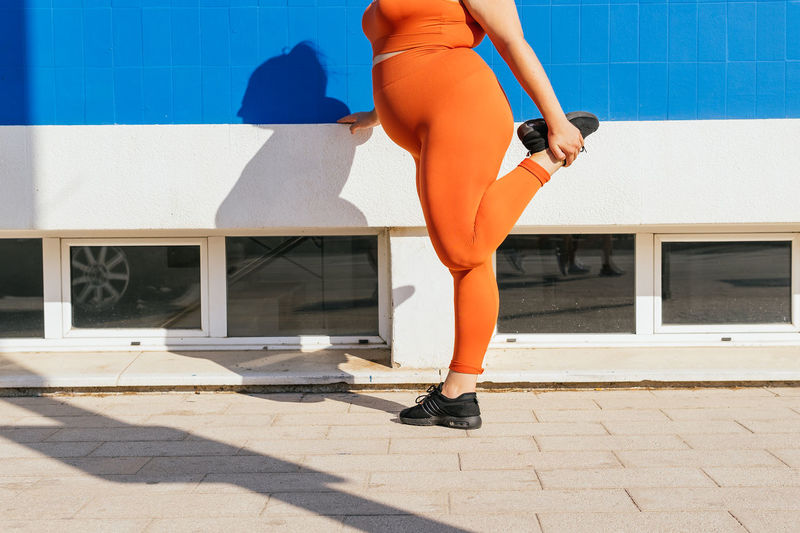 Side view of crop unrecognizable plump female athlete in sportswear exercising on tiled walkway in sunny town