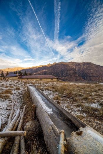 Trough over field by houses and mountains against vapor trails during winter