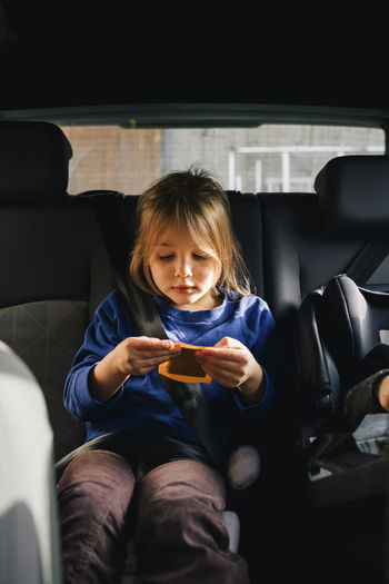 Girl holding playing card sitting at back seat in car