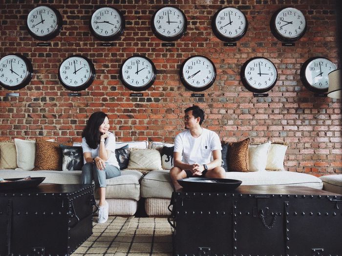 Couple sitting on sofa against wall clocks