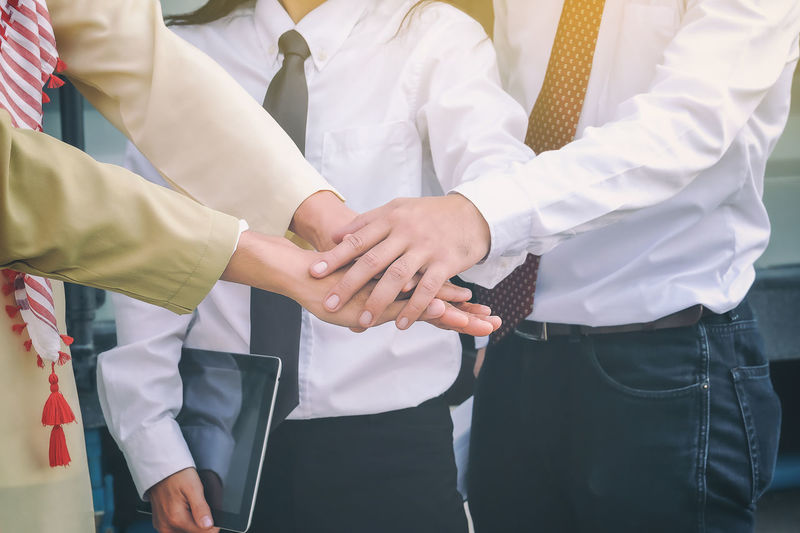 Midsection of business people huddling hands while standing outdoors