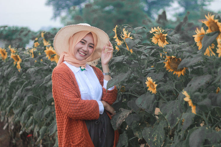 Portrait of a beautiful indonesian woman with a sweet smile standing next to a sunflower plant
