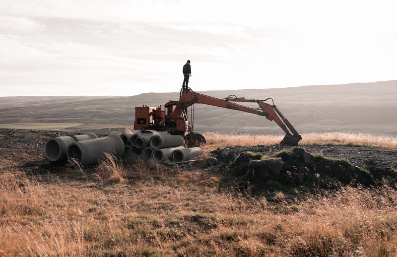 Back view of anonymous male traveler standing on abandoned excavator near reinforced concrete rings in hilly terrain in iceland