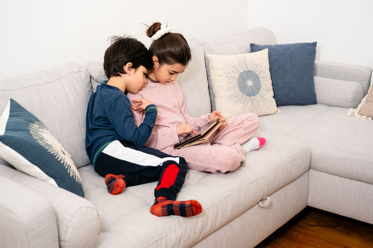 Sister using digital tablet by brother on sofa at home